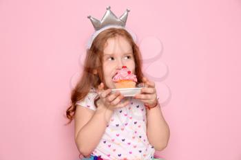 Cute little girl eating birthday cupcake on color background�