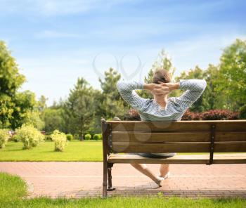 Young man relaxing on wooden bench in park�