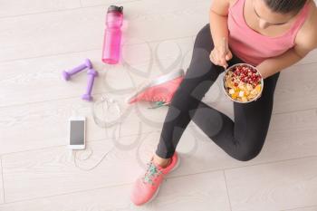 Sporty young woman sitting on floor with bowl of tasty oatmeal�