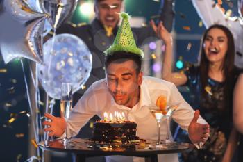 Young man blowing out candles on birthday cake at party in club�