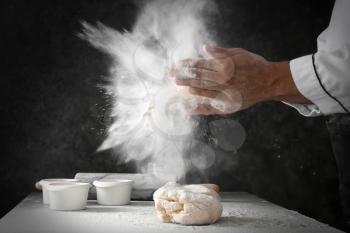 Man clapping and sprinkling flour over dough on dark background�