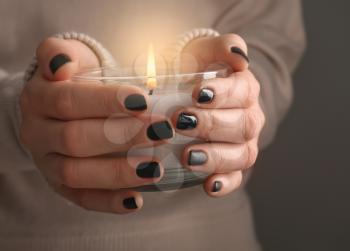 Young woman with beautiful manicure holding candle on grey background, closeup�
