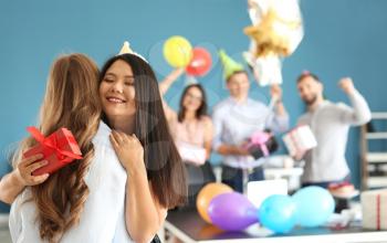 Young women with gift box hugging at birthday party in office�