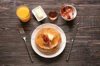 Plate with tasty pancakes and bacon on wooden table�