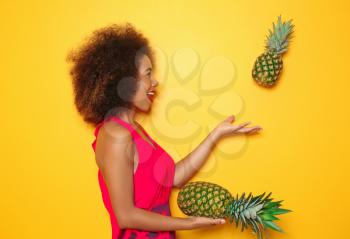 Beautiful African-American woman with pineapples on color background�