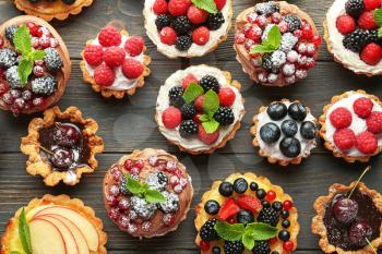 Tasty tartlets with berries on wooden background, top view�