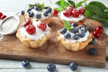Tasty tartlets with berries on wooden board�