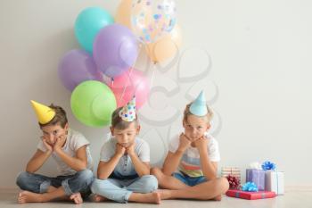 Cute little children in Birthday hats sitting on floor near light wall�