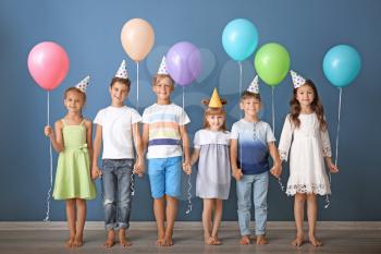 Cute little children in Birthday hats and with balloons against color wall�