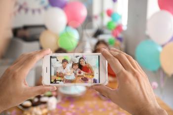 Young man taking photo of family while celebrating daughter's birthday at home�
