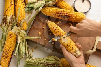 Woman cutting grilled corn cob on wooden board�