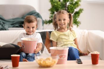 Cute children eating popcorn while watching TV at home�
