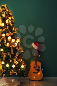 Beautiful decorated Christmas tree with guitar near color wall indoors�