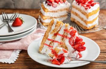 Plate with piece of delicious strawberry cake on wooden table�