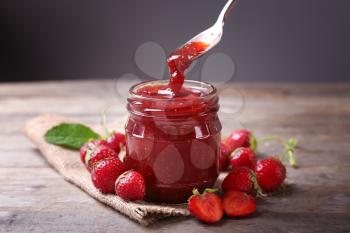 Glass jar and spoon with delicious strawberry jam on wooden table�