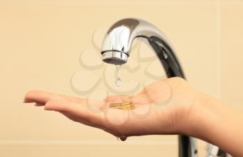 Woman holding coins under metal tap, closeup. Water saving concept�