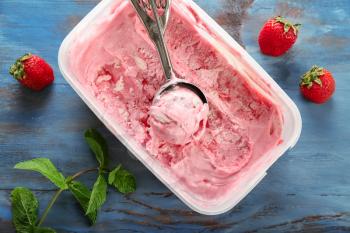 Container with delicious strawberry ice-cream on wooden background�