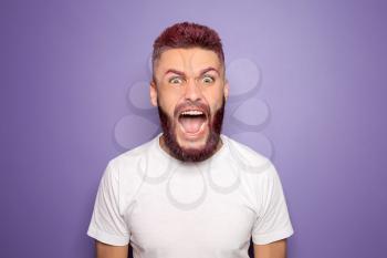 Portrait of angry screaming man with dyed hair and beard on color background�