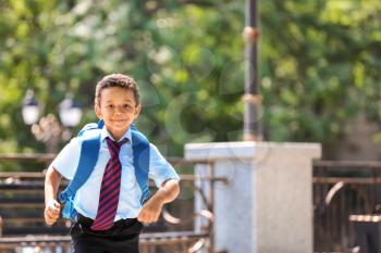 Cute African-American schoolboy running outdoors�