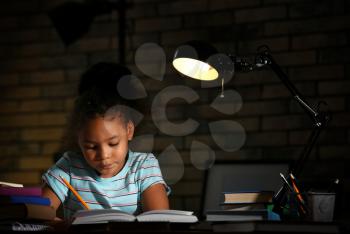 Little African-American girl doing homework in evening at home�