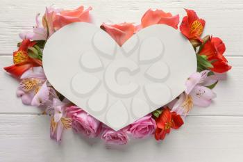 Heart shaped sheet of paper with beautiful flowers on white wooden background�