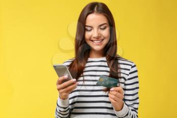 Young woman with credit card and mobile phone on color background. Online shopping�
