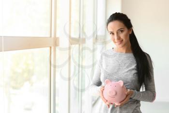 Young woman with piggy bank near window�