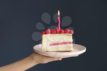 Woman holding piece of delicious birthday cake with burning candle on grey background�