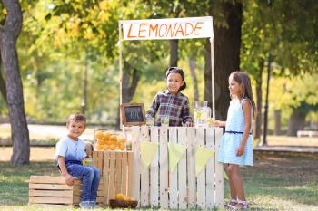 Little African-American boy selling lemonade at counter in park�