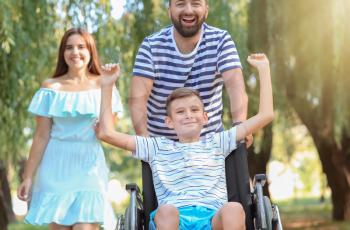 Teenage boy in wheelchair with his family walking outdoors�