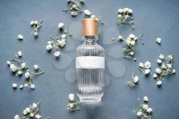Transparent bottle of perfume with beautiful flowers on grey background�