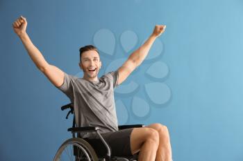 Happy young man sitting in wheelchair against color background�