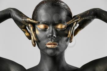 Beautiful woman with black and golden paint on her body against light background�