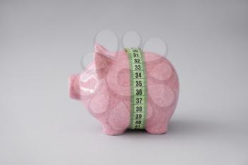 Piggy bank with measuring tape on light background. Weight loss concept�