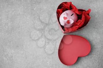 Piggy bank in heart-shaped gift box on grey background. Concept of buying presents for Valentine's day�