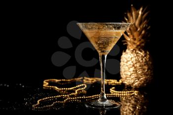 Golden cocktail with pineapple and beads on black background�