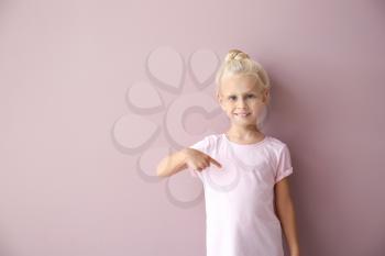 Cute little girl pointing at her t-shirt on color background�