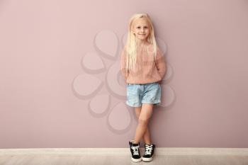 Cute girl in fashionable clothes near color wall�