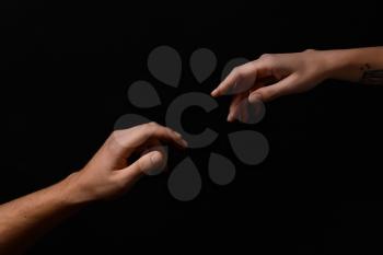 Male and female hands reaching out to each other on dark background�