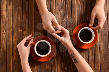 Young couple with cups of coffee holding hands on wooden table�