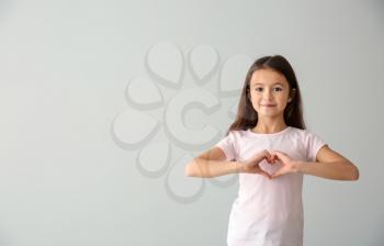 Cute girl in t-shirt making heart with her hands on light background�