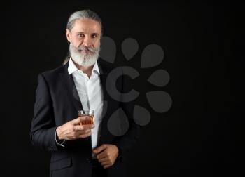 Elderly businessman with glass of whiskey on dark background�