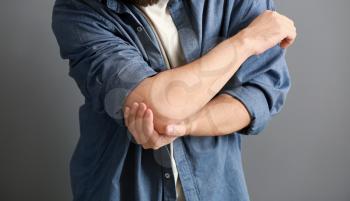 Man suffering from pain in elbow on grey background, closeup�