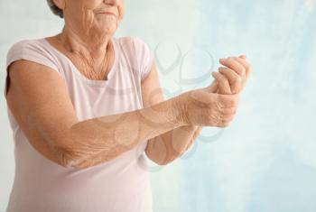 Senior woman suffering from pain in wrist on light background�