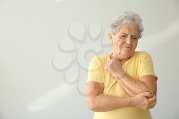 Senior woman suffering from pain in elbow on light background�