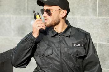 Male security guard with portable radio transmitter outdoors�