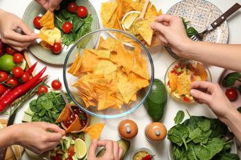 People eating tasty corn chips at white table�