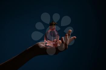 Woman holding bottle of perfume on dark color background�