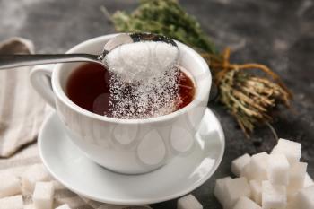 Adding of sugar to cup with aromatic tea on grey table�