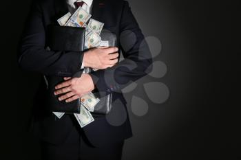 Businessman holding briefcase with dollar banknotes on dark background. Corruption concept�